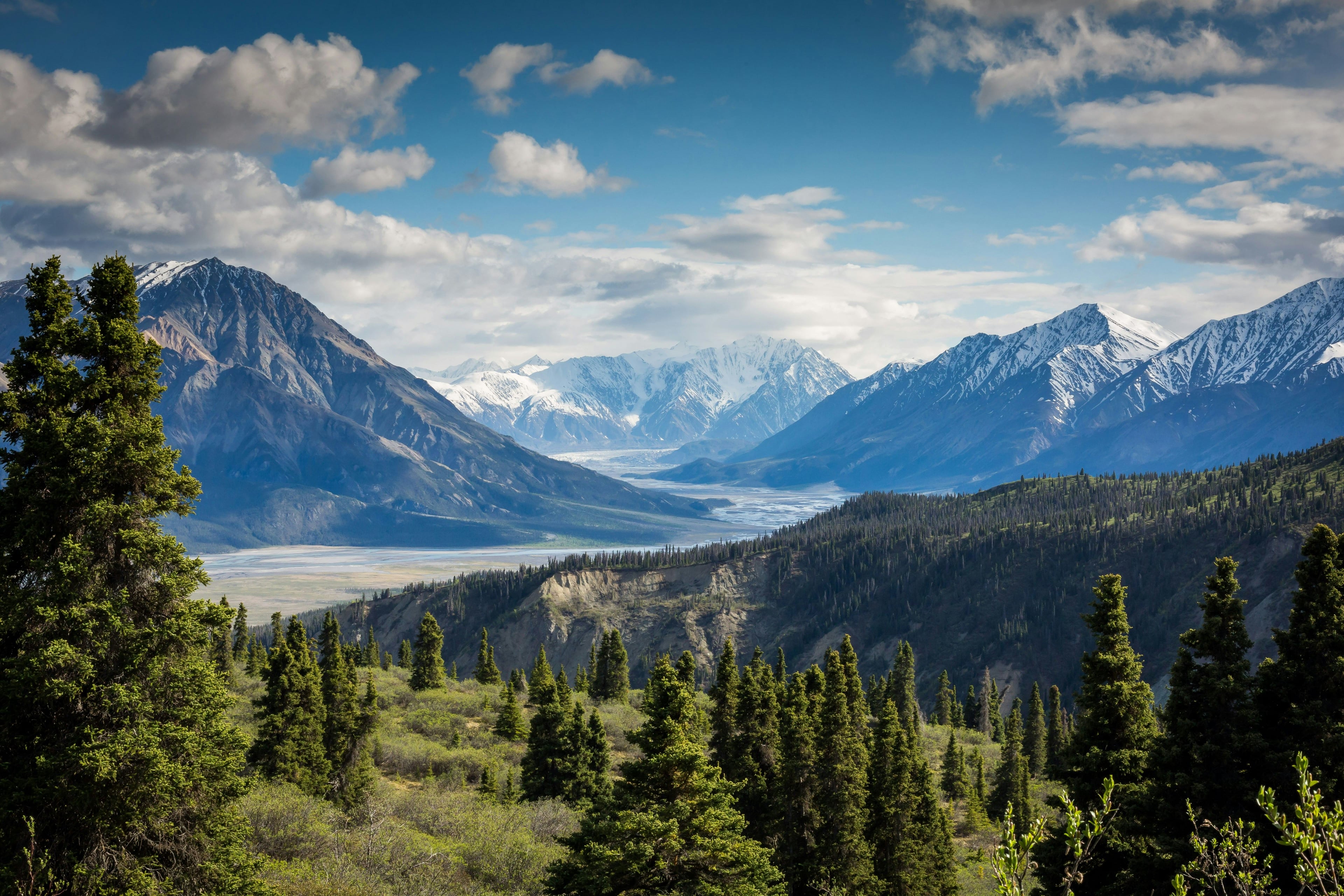 Alpine mountain landscape with snow-capped peaks, forested valleys, and glacier-fed river