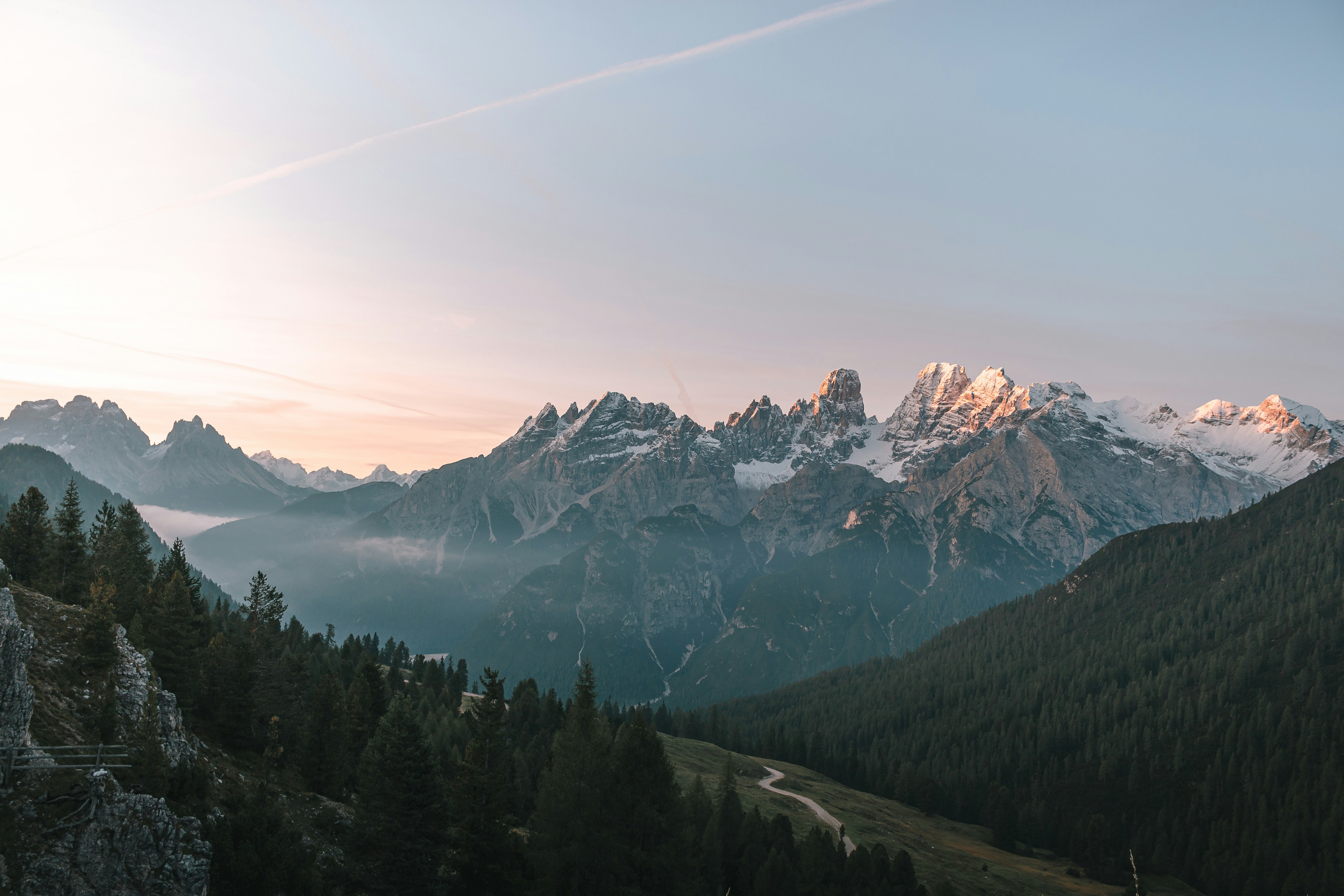 Misty Alpine mountains at golden hour with dramatic peaks and forested slopes